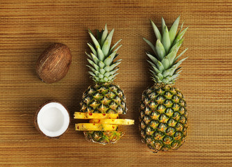 Fresh pineapples and coconuts on bamboo mat, flat lay