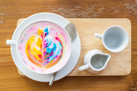 Colorful rainbow latte coffee in white cup on wooden table with copy space for text or design