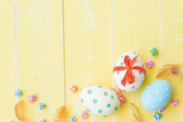 Happy easter! Colorful of Easter eggs in nest with red ribbon, Feather and paper star on pastel color bright yellow and white wooden background.