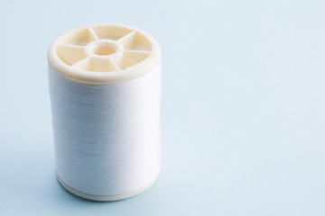 spool of  white sewing thread on blue background with copy space