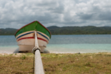 rope closeup, blurry wooden boat tied on beach -