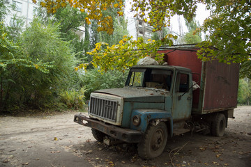 Old rusty truck with broken windows at abandoned overgrown part of town