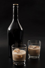 Coffee liqueur and alcoholic beverages based on milk and whiskey concept with Irish cream bottle and glasses with ice isolated on dark black background - obrazy, fototapety, plakaty