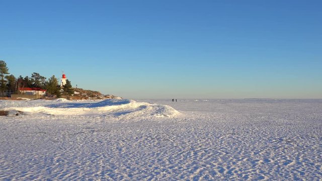 Lake frozen, unrecognizable people walking on ice near historic lighthouse, built in 1850s in late winter early spring on surface of Georgian Bay, Killarney, Ontario, Canada
