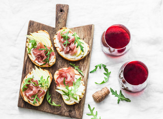 Bruschetta with cream cheese, pear, prosciutto, arugula on wooden chopping board and red wine  on...