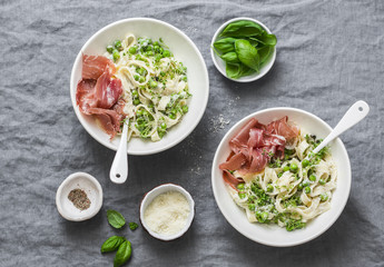 Lunch table in mediterranean style. Fettuccine pasta with creamy sauce, green peas and prosciutto on grey background, top view