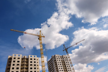 Fototapeta premium Tower cranes and unfinished multi-storey high near buildings under construction site in the sunny day with beautiful clouds