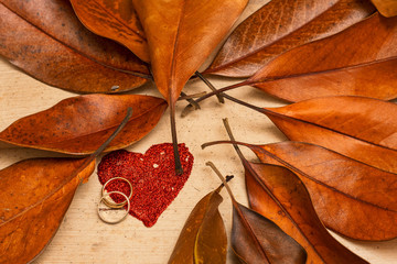 stract heart with wedding rings surrounded by autumn leaves