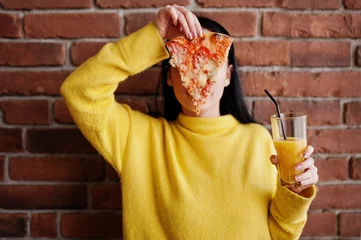 Fototapete Pizzeria Funny brunette girl in yellow sweater eating pizza at restaurant.
