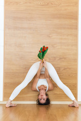Sporty beautiful young woman in a white suit practicing yoga, holds tulips, doing Standing Straddle...