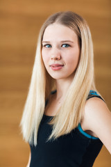 Naklejka premium Portrait of positivity and pretty blonde girl in black sportwear smiling at camera and posing, holds hand on waist in the gym. Concept of sport and healthy lifestyle. wooden background
