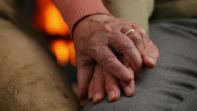 Senior hands of woman and man in front of the fireplace - comforting each other at old age concept, camera slide