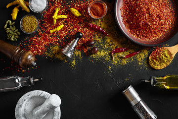 Fototapeta na wymiar Cooking using fresh ground spices with mortar and small bowls of spice on a black table with powder spillage on its surface, overhead view with copyspace