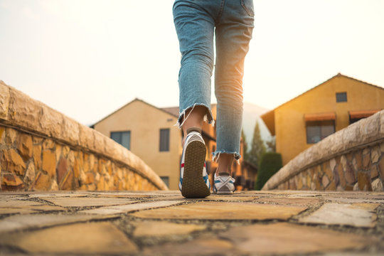 Woman jeans and sneaker shoes walking on the brick bridge to the village with sunlight