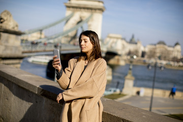 Young woman holding mobile phone with Chain bridge in background in Budapest