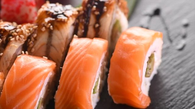 Sushi roll set on black slate background. Rotated California set with salmon, tuna, eel, flying fish caviar closeup. Japan restaurant menu. 4K UHD video footage. 3840X2160