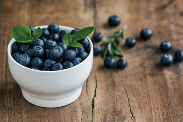 Fresh blueberries heap in white bowl in side view with copy space on wood table for background in vintage tones. Blueberry is healthy and delicious fruits which have high antioxidant and vitamin C.