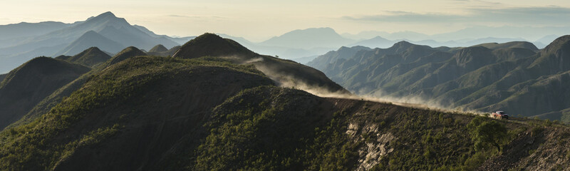 panorama of our Mitsubishi pick-up driving over the crest of beautiful green hills followed by a dust cloud trail at Torotoro National Park - obrazy, fototapety, plakaty