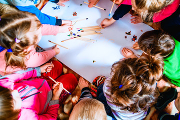 several small children draw on a sheet of paper with pencils. A view from above.
