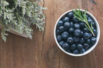 Fresh ripe wild blueberries in white bowl on rustic wood table in top view flat lay with copy space for background. Blueberry is antioxidant food and vitamin C. Healthy and delicious fruits concept.