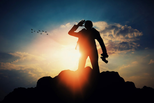 silhouette of businessman with binocular for searching a opportunity on top of mountain against sun light