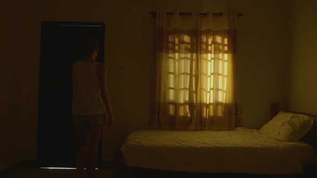 A woman opens the door in a dark room and the room is filled with bright light