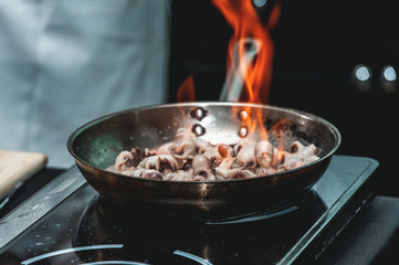 The chef cooks the small octopus on a metal frying pan