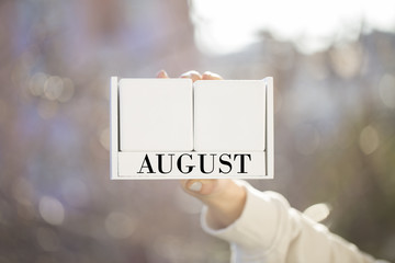 the woman is holding a white wooden calendar. white wooden cube shape calendar for august with hand 