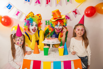 clown girl and clown boy at the children's birthday party. Festive table with a beautiful cake. Blow out candles and make a wish