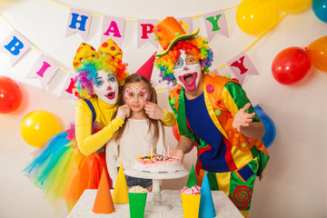 clown girl and clown boy at the children's birthday party. Festive table with a beautiful cake. Blow out candles and make a wish