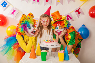 clown girl and clown boy at the children's birthday party. Festive table with a beautiful cake. Blow out candles and make a wish