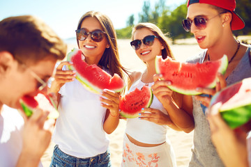 Group of friends having fun eating watermelon. on the beach. Excellent sunny weather. Beautiful figures. Super mood. Summer concept.