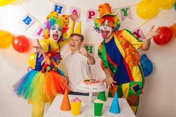 clown girl and clown boy at the birthday party of an adult guy. Festive table with a beautiful cake. Blow out candles and make a wish