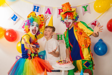 Obraz na płótnie Canvas clown girl and clown boy at the birthday party of an adult guy. Festive table with a beautiful cake. Blow out candles and make a wish