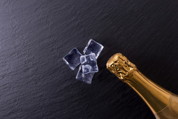 Champagne bottle and ice cubes on black slate plate with copy space