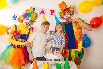 clown girl and clown boy at the birthday of a little girl and her big brother. Festive table with a beautiful cake. Blow out candles and make a wish