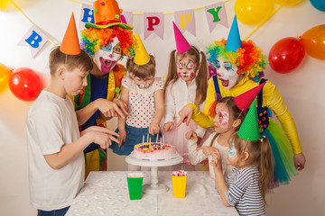 clown girl and clown boy at the children's birthday party. Festive table with a beautiful cake. Blow out candles and make a wish