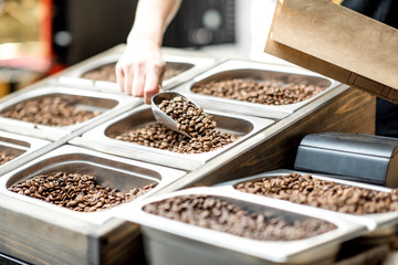 Filling paper bag with coffee beans from the metal trays for selling in the store