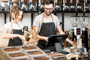 Two sellers in uniform filling bags with coffee beans while working in the coffee store