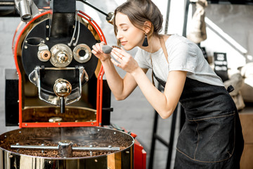 Woman checking the quality of the coffee beans standing with scoop near the roaster machine at the...