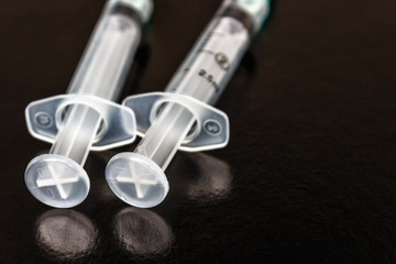Medical syringes of different capacities lie on a black glossy surface.