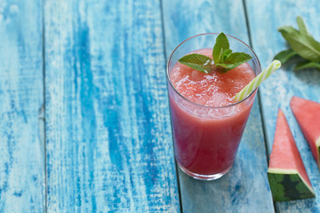 Fresh watermelon cocktail in a glas with mint on the top on a blue wooden rustic background with copyspace