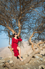 Fototapeta premium Beautiful girl in red dress bellow desert tree