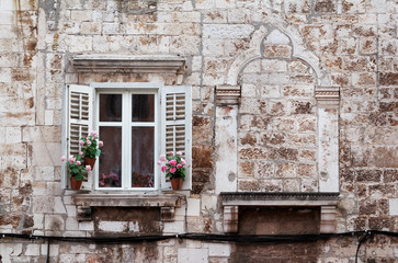 Fototapeta na wymiar Aged windows and flower boxes of historical building from old town of Pula, Croatia / Detail of ancient venetian architecture with decorative elements / Material, texture, background and wallpaper.