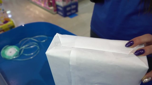 Young woman wrapping Christmas presents with white paper in a toy store