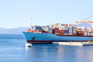 Container ship for carriage of goods with containers to shore in port ship port on horizon / Cargo transportation by sea and goods unloading process / Business logistics and transportation concept.