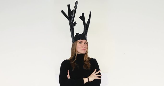 Beautiful young woman putting a fantastic black paper crown from scoop and cardboard on her head and laughter on the white background