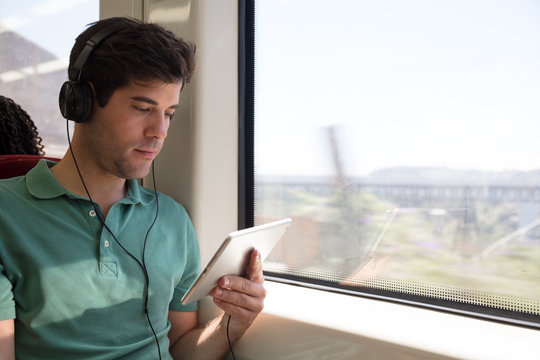 Young man with headphones and tablet computer in train