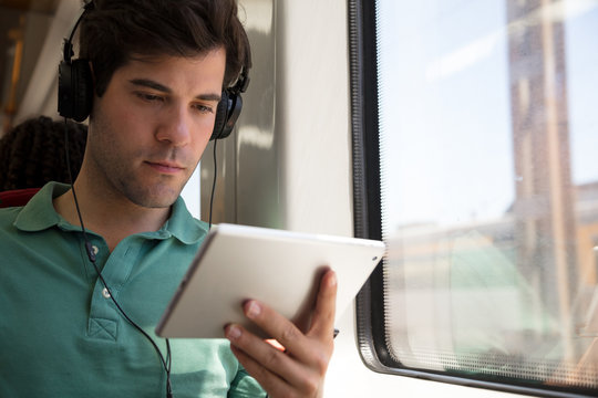 Young man with headphones using a digital device on a train