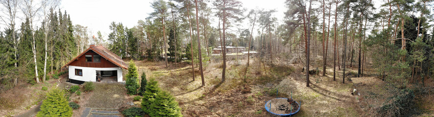 Composite panorama from aerial photos with a drone in low heights, detached house from the seventies on a forest property, old broken trampoline for the children